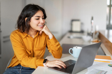 Distance Job. Smiling Young Arab Woman Working With Laptop In Kitchen