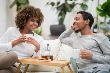 Cheerful african american husband and wife drinking tea at home