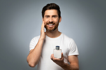 Grooming and people concept. Happy handsome caucasian man applying perfume on beard, grey studio...