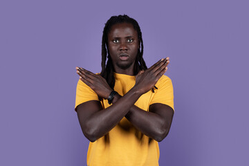 Serious african american millennial guy in casual saying no, looking at camera and showing hands crossed over chest, blue studio background, copy space. Human gestures concept