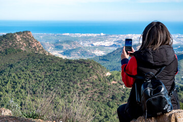 Joven mujer tomando fotos con su teléfono móvil desde lo alto de la montaña.