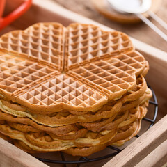 Pile of fresh homemade heart shaped waffles on wooden tray (Selective Focus, Focus on the front edge of the top waffle)