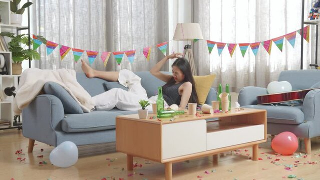 Drunk Asian Woman Wakes Up After Sleeping On A Sofa And Holding Her Head With Hands Due To Having A Headache In The Party Room At Home
