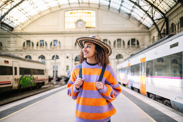 Young black woman traveler with backpack and hat at the train station with a traveler.