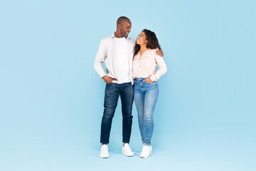 Full length shot portrait of black couple hugging and looking at each other, posing on blue background, full body length