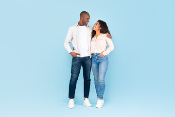 Full length shot portrait of black couple hugging and looking at each other, posing on blue...