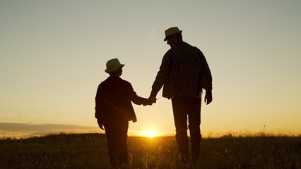 Fototapeta na wymiar Father and son walk together holding hands in park at sunset. Silhouette, happy family, baby dad travel to sunset. Childhood dream, fatherly. Dad plays with his kid outdoors in park. Child adolescence