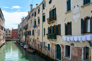 Fototapeta na wymiar Picturesque facades of old buildings with hanging clothes and boats parked on canal in Venice, Italy, under blue sky with clouds on spring day. Beautiful view in famous Italian landmark.