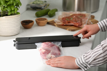 Woman using sealer for vacuum packing in kitchen, closeup. Sous vide cooking