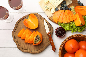 Delicious persimmon, blue cheese, blueberries and jam served on white wooden table, flat lay