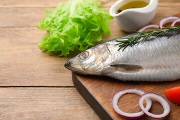 Board with delicious salted herring and ingredients on wooden table, closeup. Space for text