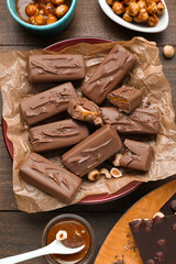 Delicious chocolate candy bars and nuts on wooden table, flat lay