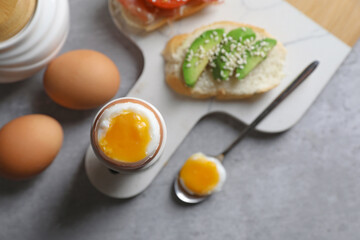 Fresh soft boiled egg in cup and sandwich with avocado served on grey table, flat lay