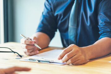 Closeup businessman hands working on finance business document reading report paperwork spreadsheet using laptop at office desk. Man hands write on office note look at financial graph chart document