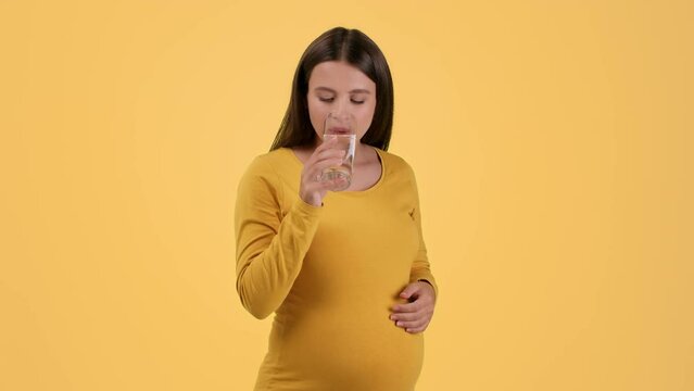 Healthcare during pregnancy. Young pregnant woman taking vitamin pill and drinking water, smiling to camera, free space