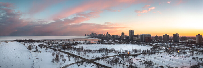 Beautiful Chicago winter skyline aerial above a snow covered Montrose beach looking towards the downtown skyscraper buildings with pink and orange clouds in a blue sky above.