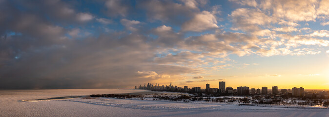 Wide angle aerial panorama of the north side of Chicago from above the frozen water of Lake Michigan overlooking the Uptown and Lakeview neighborhoods towards downtown at sunset with cloudy sky above.