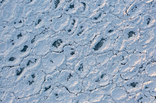Close up top down aerial drone shot of rounded ice chunks covered in white snow floating on the icy waters of Lake Michigan making a beautiful textured winter background with copy space.