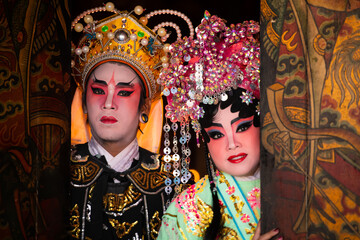 Portrait of male and female opera performers at the entrance to a sacred shrine or temple, praying...
