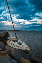 Abandoned sailboat moored at the jetty of Provincetwon Causeway in Cape Cod Bay, Massachusetts, USA, oceanside beach seascape and dramatic cloudscape in Provincetown at twilight