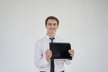 A handsome young man using his laptop and showing it to the camera on a gray background with a space to copy. Layout for creating your design. High quality photo