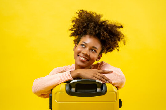 Portrait of young attractive traveling african american woman curly hair with baggage in studio on yellow background.