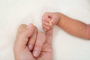 newborn baby holding little finger of mother's hand on bed