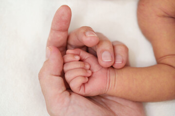 mother holding newborn baby hand on bed