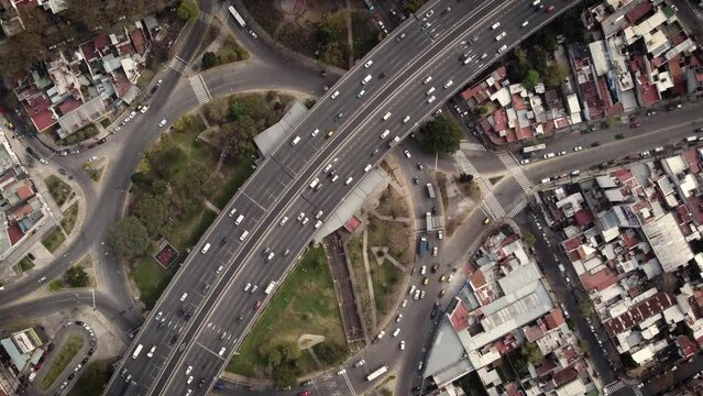 A stationary timelapse aerial shot of heavy traffic over and under the flyover. The expressway above is congested while the roads and roundabout below has light traffic and moving easily.