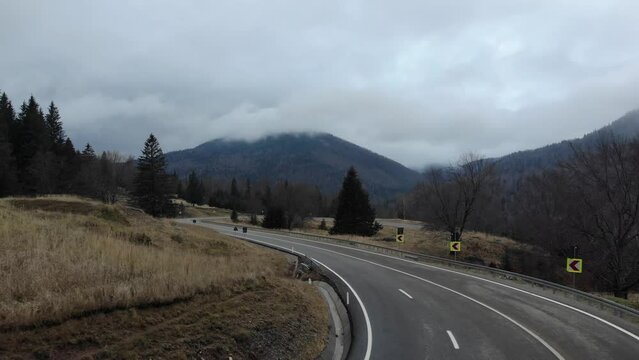 Empty Concrete Road Through Sloping Mountains Under Gloomy Sky. Aerial Drone Shot