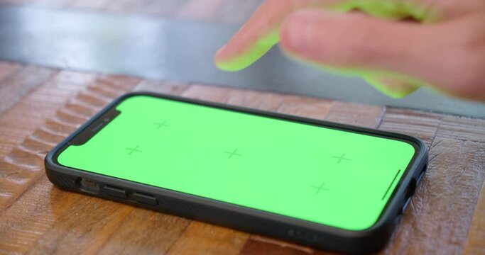 Iphone lying flat on a table, screen displayed in close-up, with green screen for replacement. Footage shows phone being tapped and swiped. Perfect for showcasing technology.