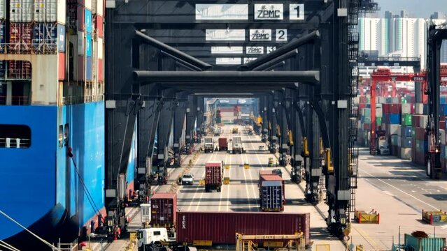 Truck carrying a container turns into a lane under the container cranes in the port of Hong Kong while loading the giant vessel. Drone dolley Pull-away shot