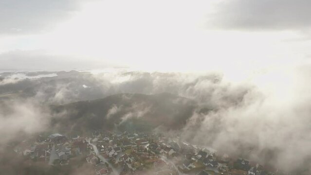 Drone footage of housing estate in Norway with some fog floating in th air and sun lighting up the clouds