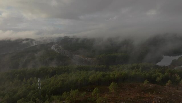 Drone footage of highway, radiotower, and housing estate in Norway with some fog floating in the air and sun lighting up the clouds