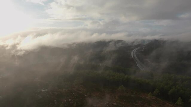 Drone footage of a radio tower and housing estate in Norway with some fog floating in the air and sun lighting up the clouds