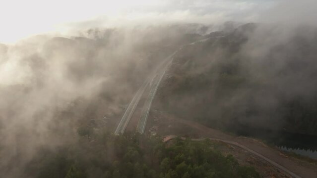 Drone footage of highway, and housing estate in Norway with some fog floating in the air and sun lighting up the clouds
