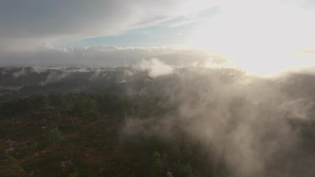 Drone footage of a radio tower and housing estate in Norway with some fog floating in th air and sun lighting up the clouds