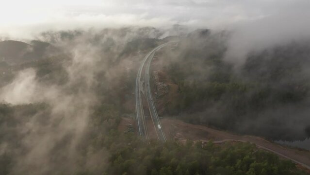 Drone footage of highway, and housing estate in Norway with some fog floating in the air and sun lighting up the clouds