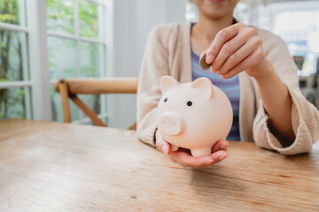 Hand of woman putting coin into piggy bank on a wooden table with blue background. saving money and invest concept.