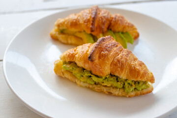 Croissant sandwich with egg,avocado on white dish and honey, coffee. breakfast and healthy food concept..