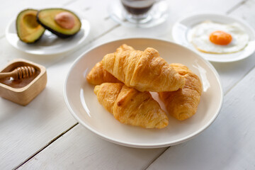 Croissant sandwich with egg,avocado on white dish and honey, coffee. breakfast and healthy food concept..