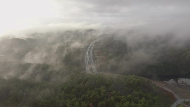 Drone footage of highway, and housing estate in Norway with some fog floating in the air and sun lighting up the clouds