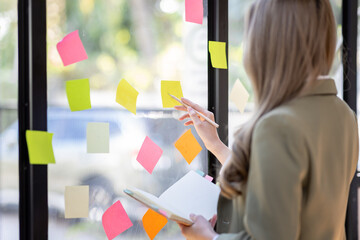 Business female employee with many conflicting priorities arranging sticky notes commenting and...