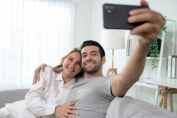 Fototapeta premium Caucasian couple video calling talking with friends on mobile phone in living room. 