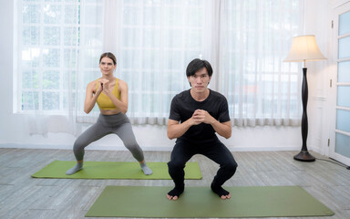 Young Caucasian woman and Asian man exercising and meditating by doing yoga together at home.