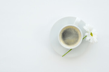 Cup of coffee and chamomile flower on a white background, top view, copy space. Morning coffee and flower