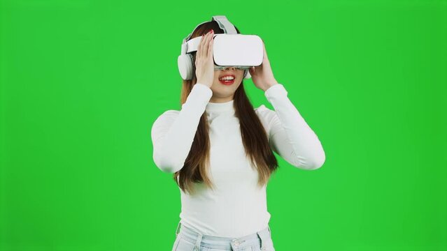 Virtual Reality concept. Front view of a young asian woman looking around, wearing a white shirt and a VR headset, greenscreen