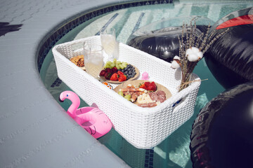 A view of a basket of catered snacks, floating on the surface of a swimming pool.