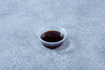A view of a plastic condiment cup of soy sauce.