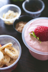A closeup view of a strawberry yogurt and sides of toppings.